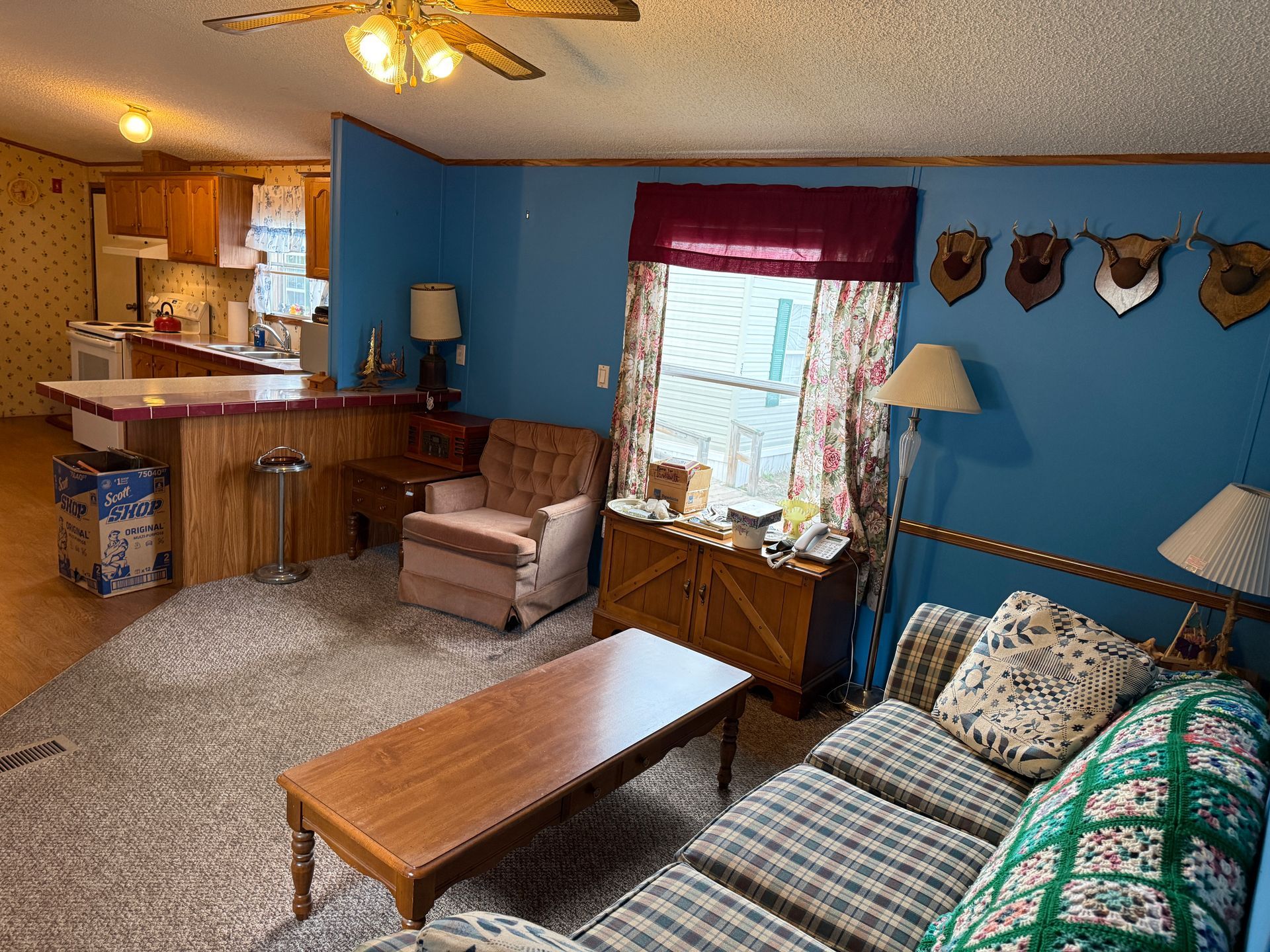 Cozy living room with blue walls, striped sofa, wooden coffee table, and open kitchen in the background