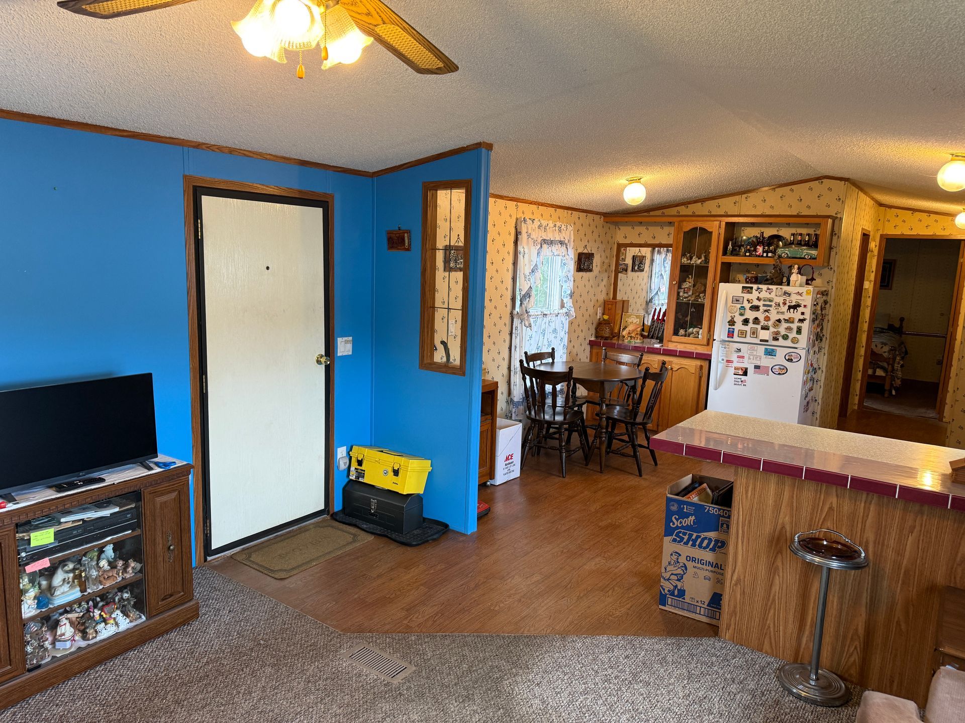 Living room and kitchen area with blue accent wall, white door, wood floor, and ceiling fan