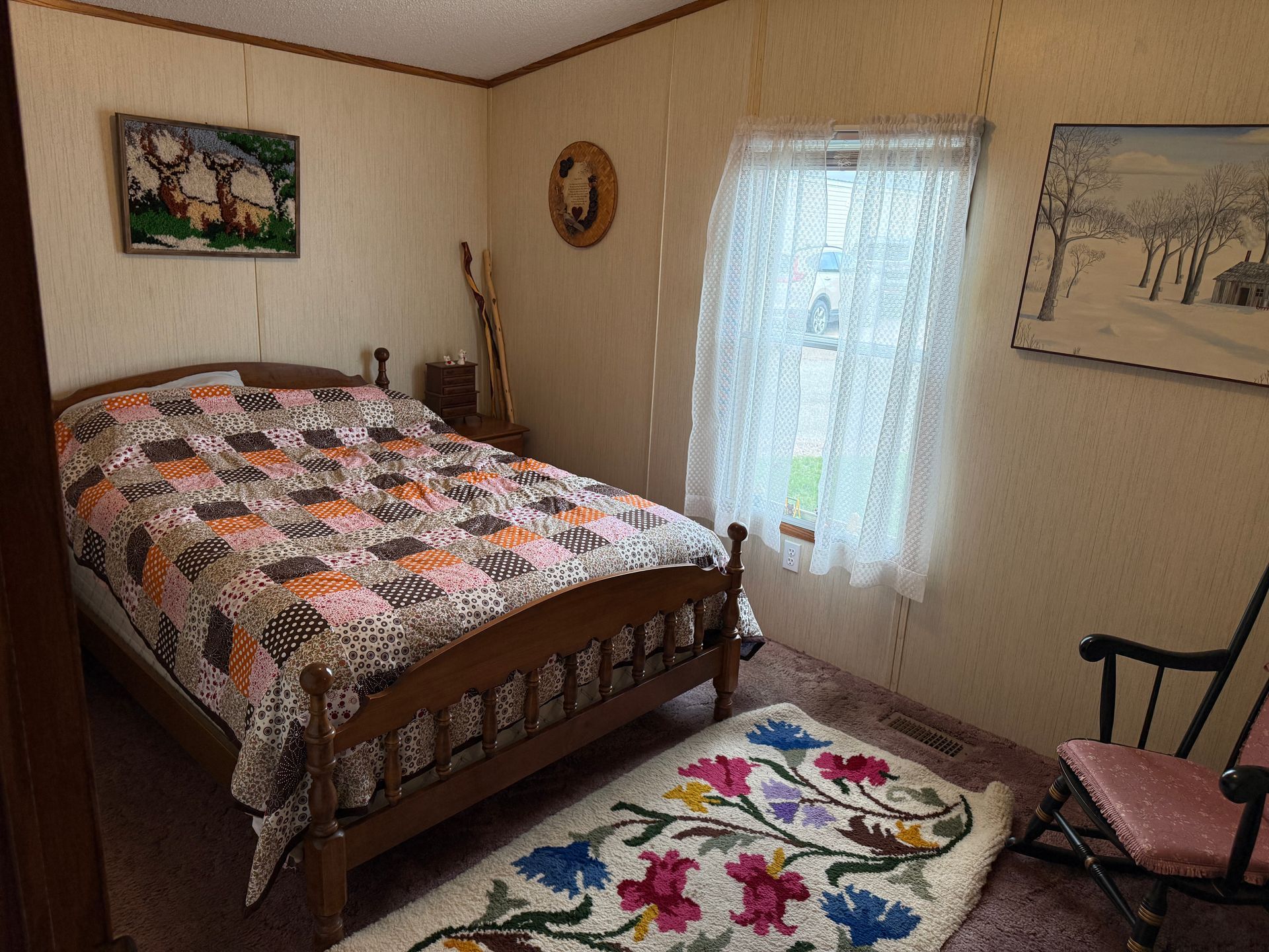 Small bedroom with a bed, floral rug, window, and framed wall art.