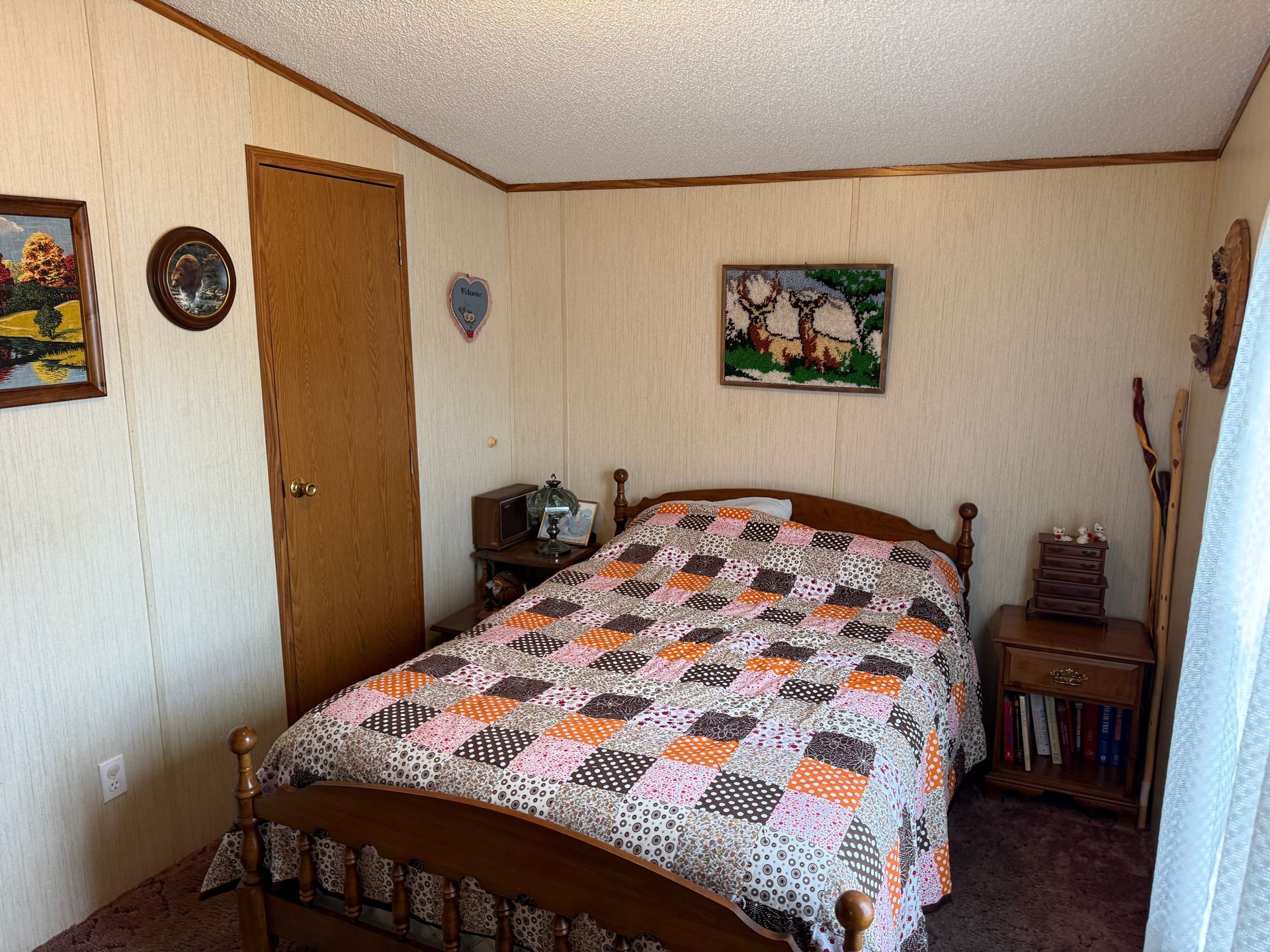 Small bedroom with a bed, wooden door, nightstand, wall art, and patterned quilt.