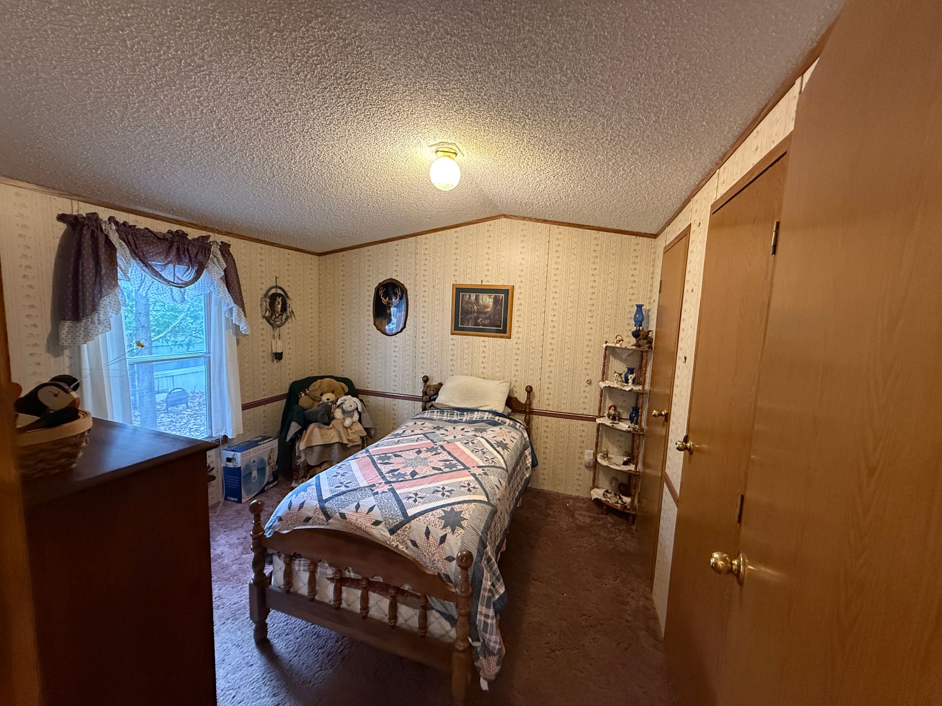 Cozy bedroom with a wooden bed, patterned quilt, dresser, and curtained window under a vaulted ceiling