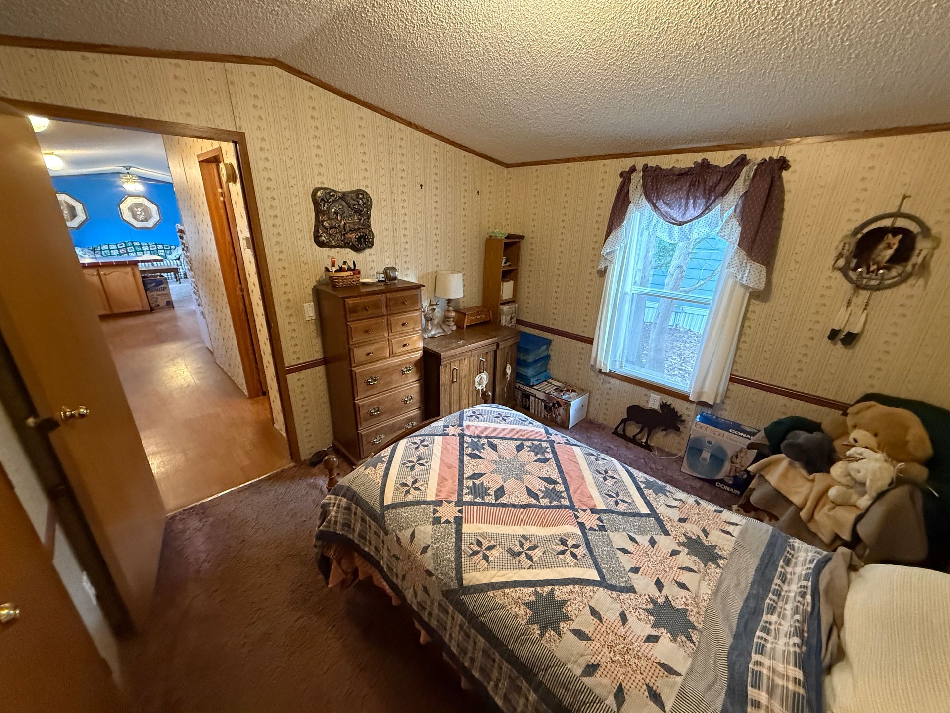Cozy bedroom with quilted bed, dresser, teddy bear, and window with curtains