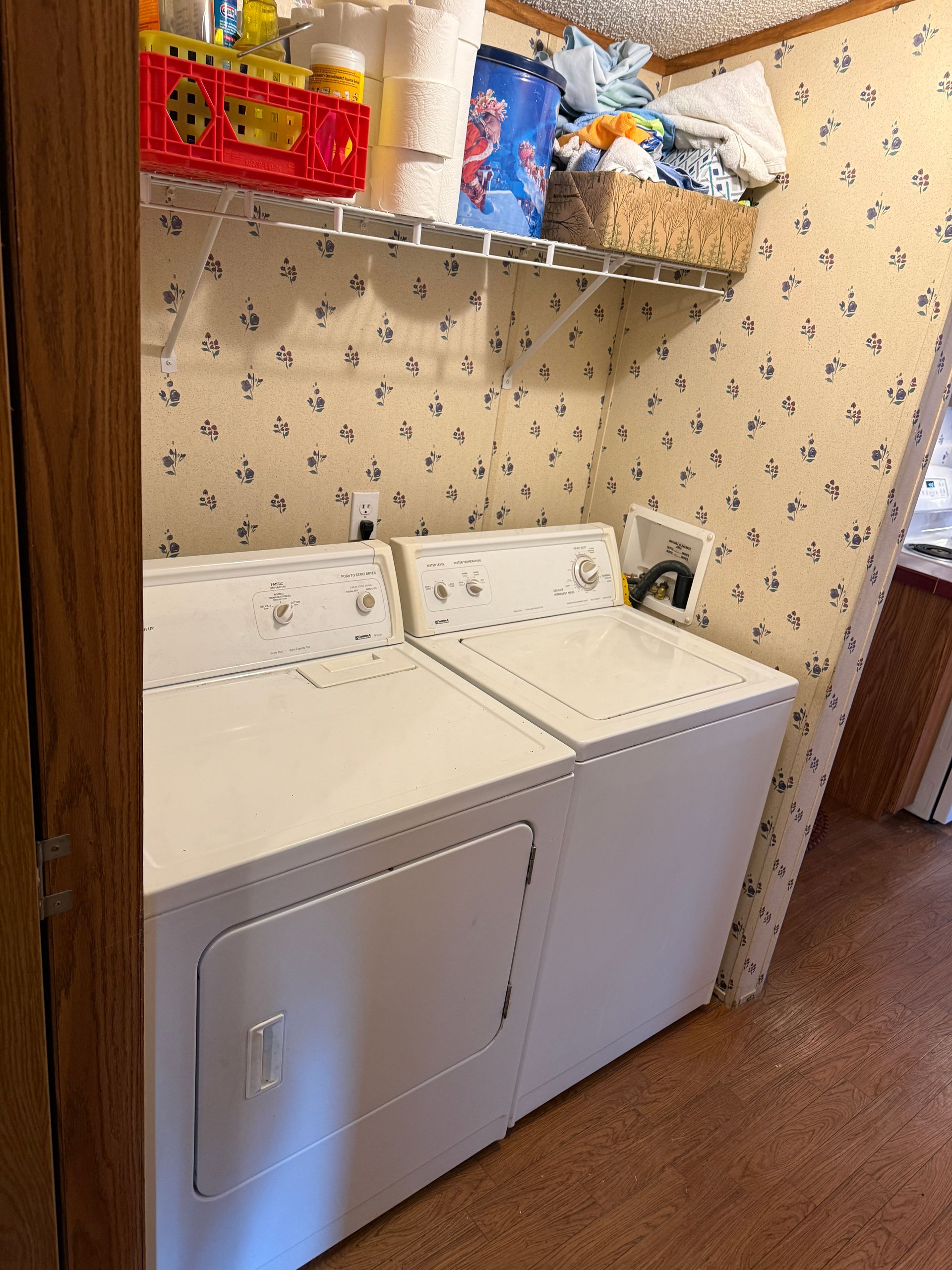 Laundry room with a washer, dryer, and overhead shelves holding cleaning supplies.