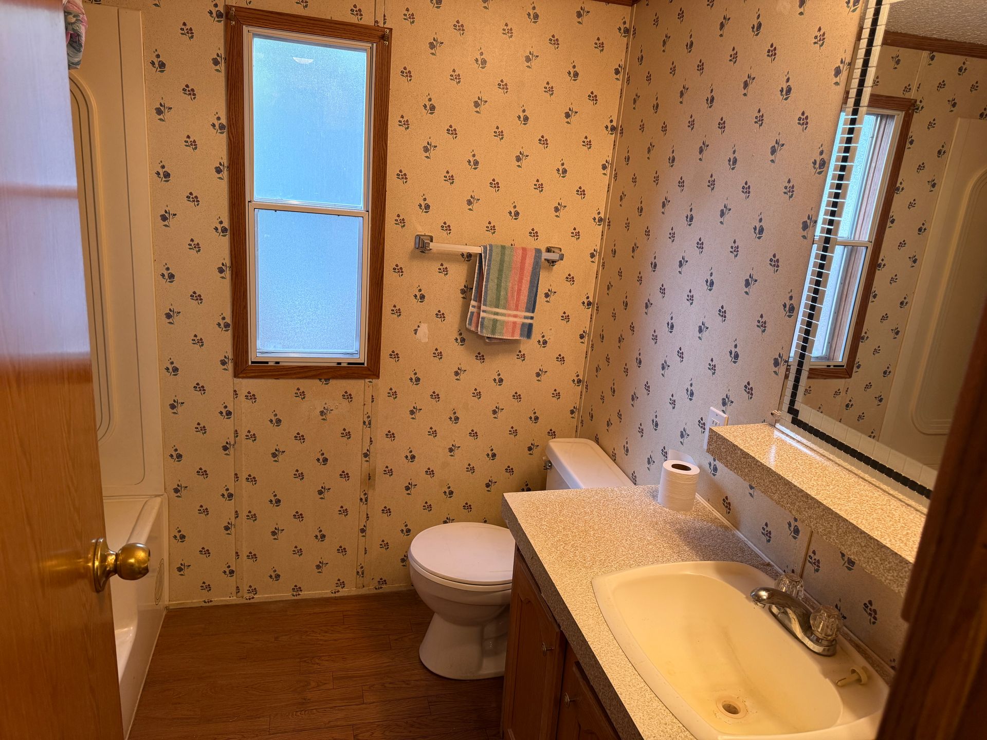 Small bathroom with patterned wallpaper, toilet, sink vanity, mirror, and narrow windows.