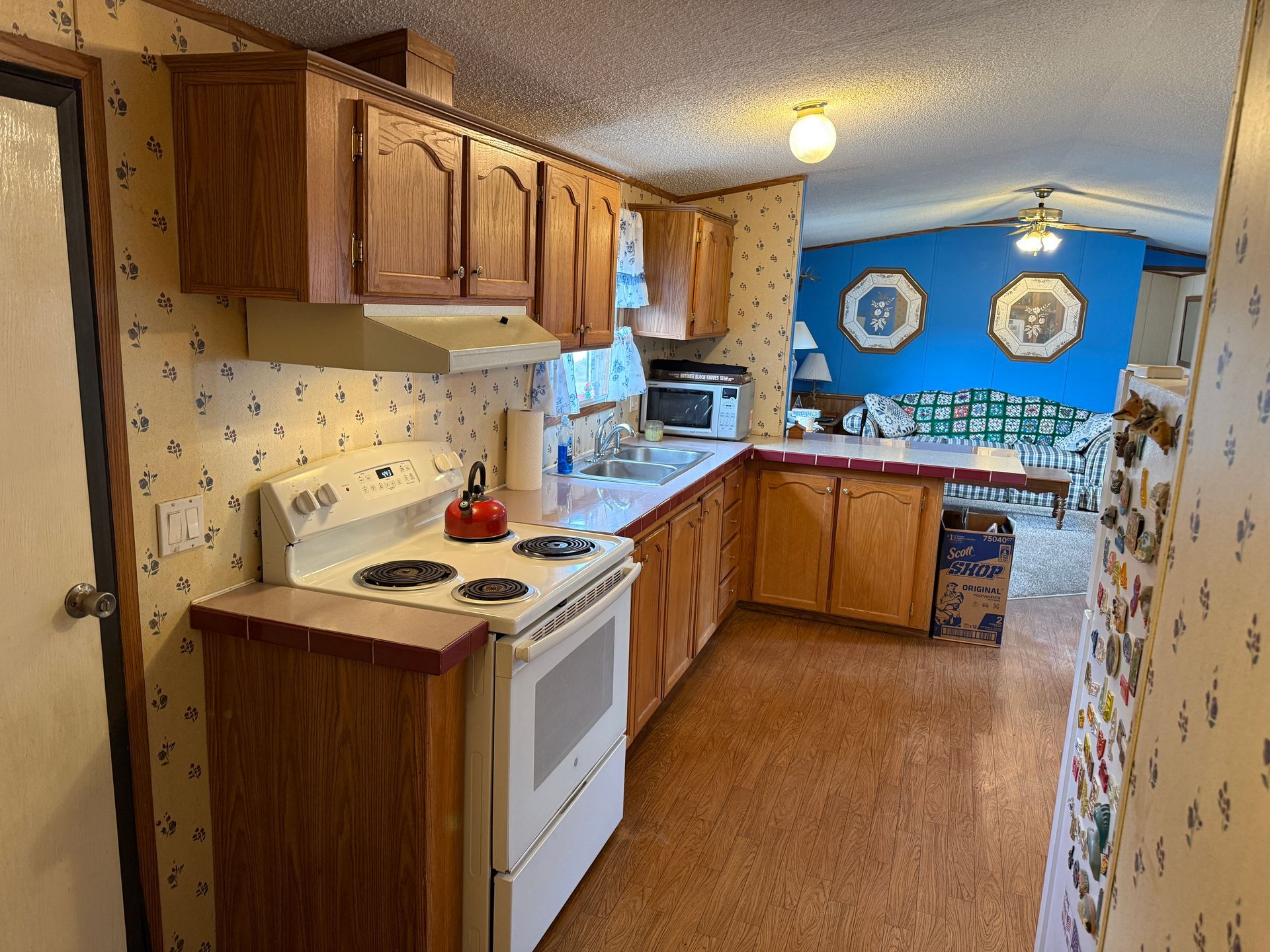 Long, narrow kitchen with wood cabinets, white appliances, and blue dining area at the end