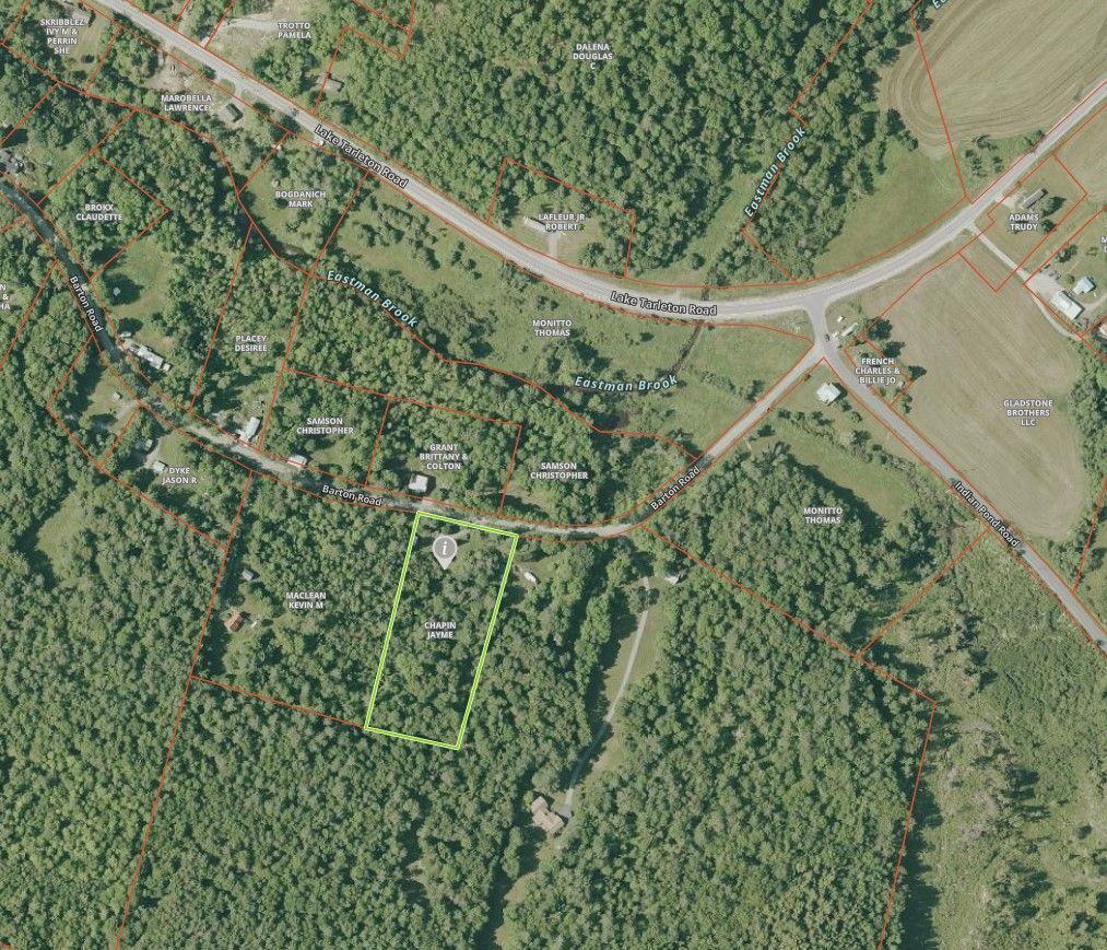 Aerial satellite view showing a plot of land outlined in green amidst a wooded area and nearby roads.