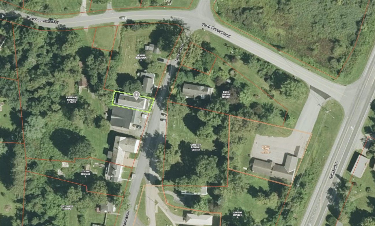 An aerial view shows a rural residential area with houses, surrounding trees, and intersecting paved roads.