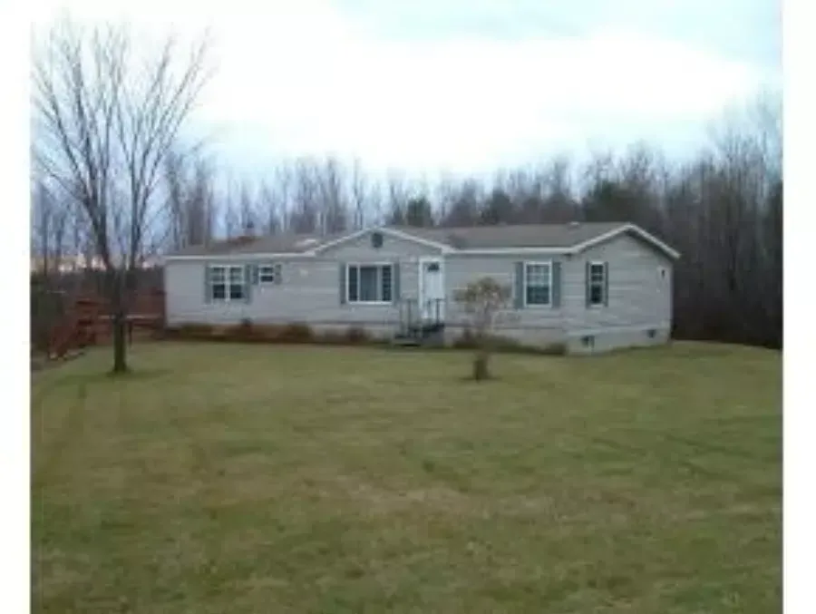 Single-story gray house with white trim on a large grassy lawn, framed by leafless trees.