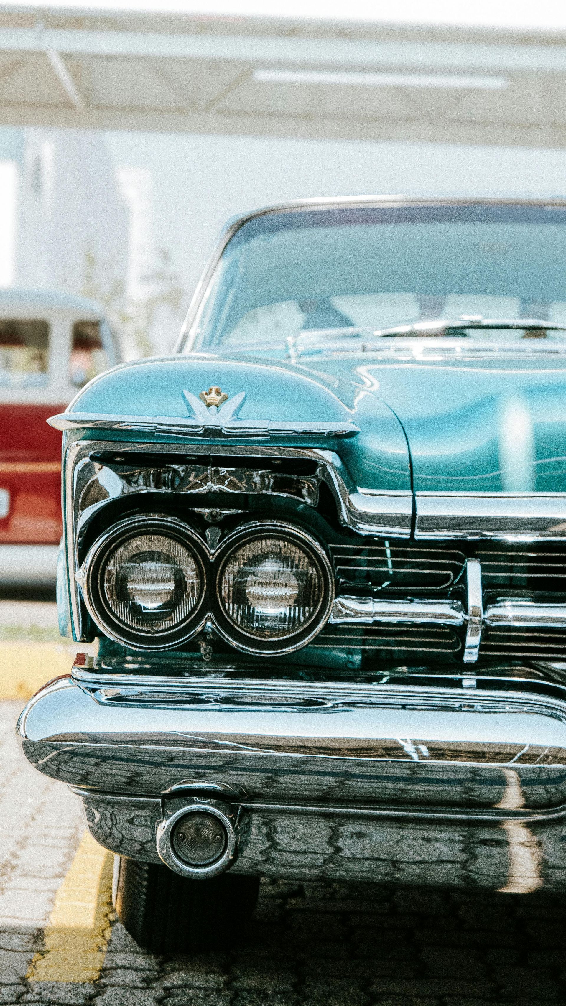 Front view of a turquoise classic car with chrome grille and round headlights, parked outdoors.