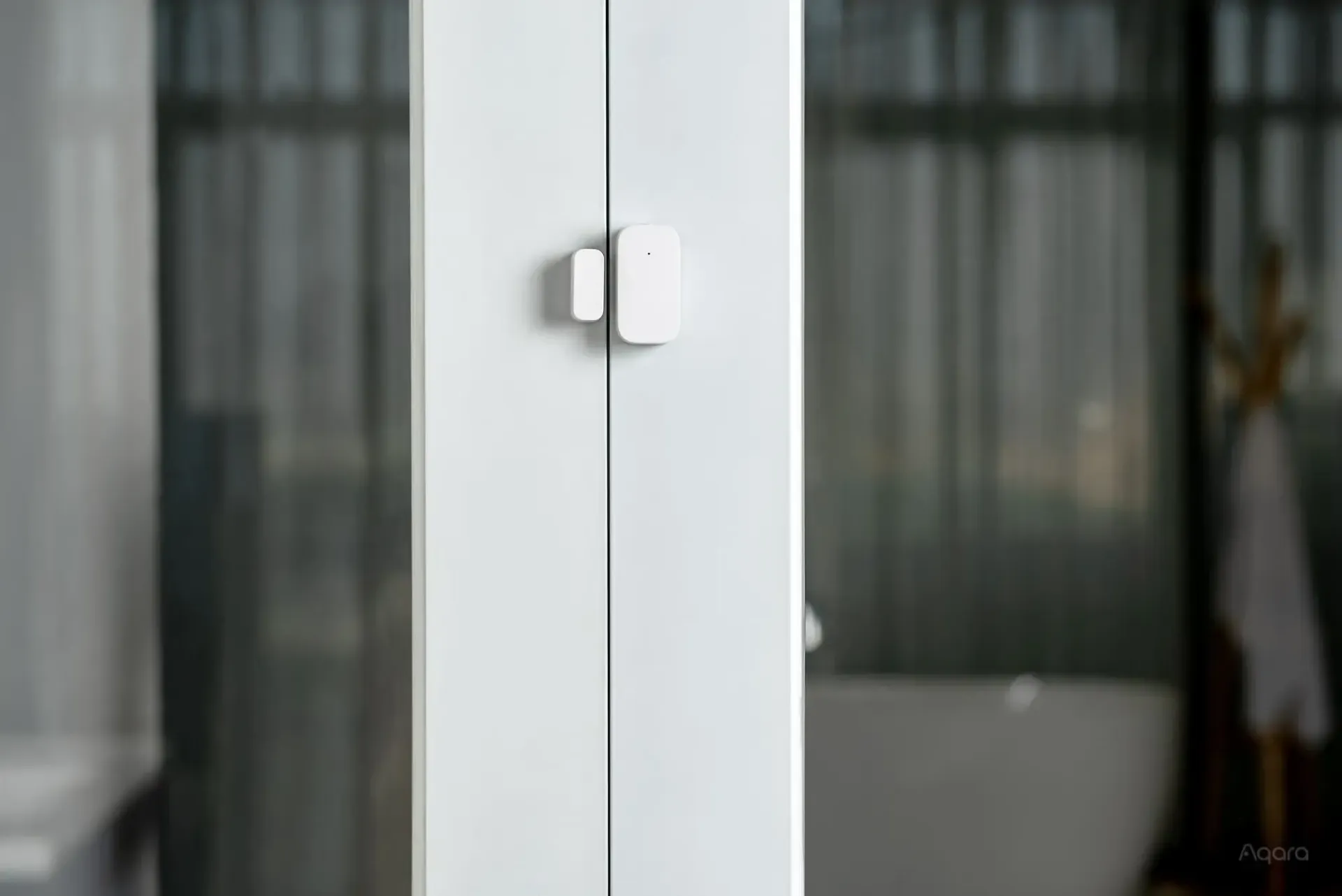 Un capteur de porte blanc est fixé à une porte vitrée dans une salle de bain.