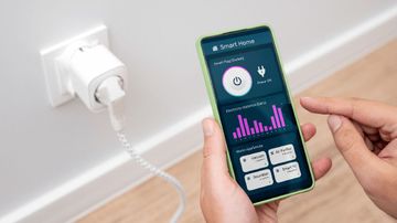 Personne utilisant un smartphone pour contrôler une prise intelligente, surveillant la consommation d'énergie ; mur blanc.