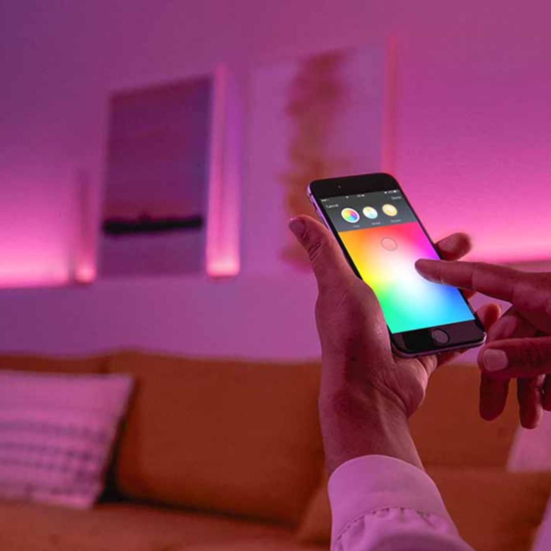 Une personne utilise son smartphone pour contrôler des rubans LED colorés. Ambiance salon.