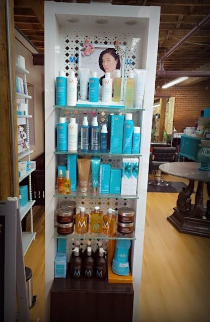 Shelf display of Moroccanoil hair products in a salon. Teal and brown bottles, jars on glass shelves.