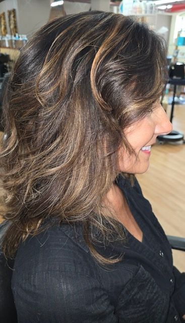 Woman with layered brown hair, highlighted with lighter tones, in a salon setting.