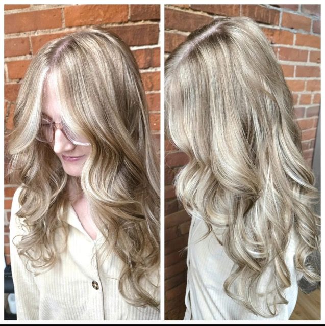 Woman with blonde hair styled in loose waves, wearing a cream-colored shirt, in front of a brick wall.