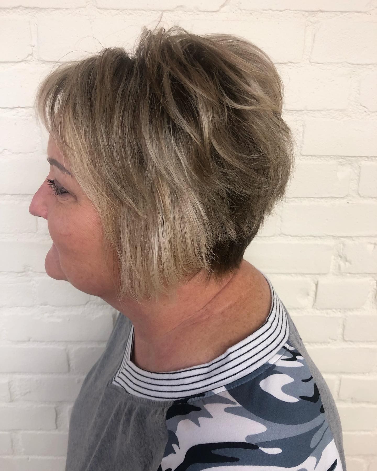 A woman with short blonde hair is wearing a camouflage shirt.