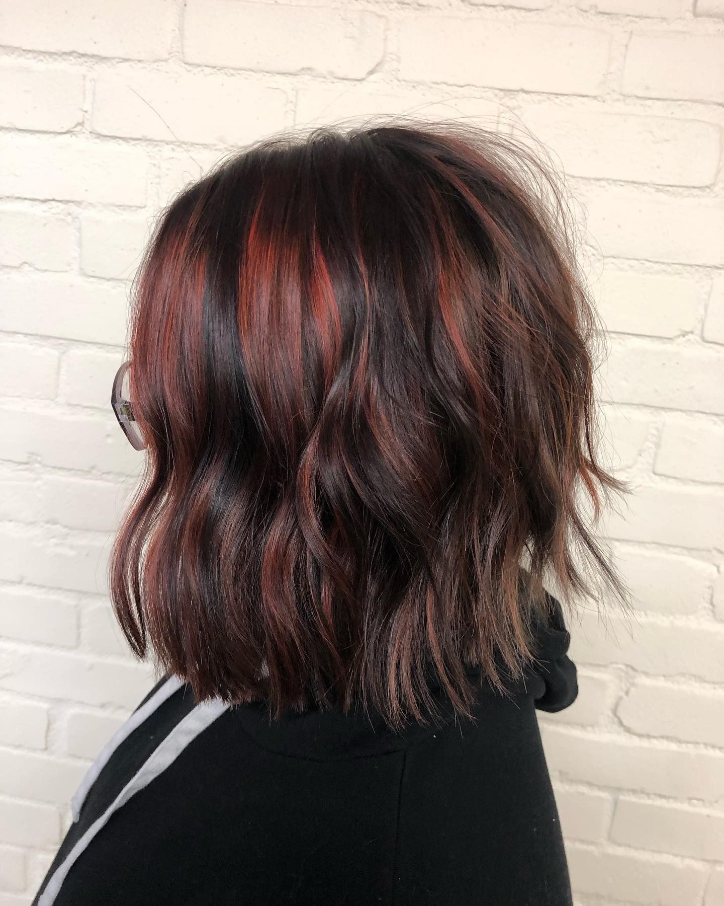 A woman with red hair and glasses is standing in front of a white brick wall.