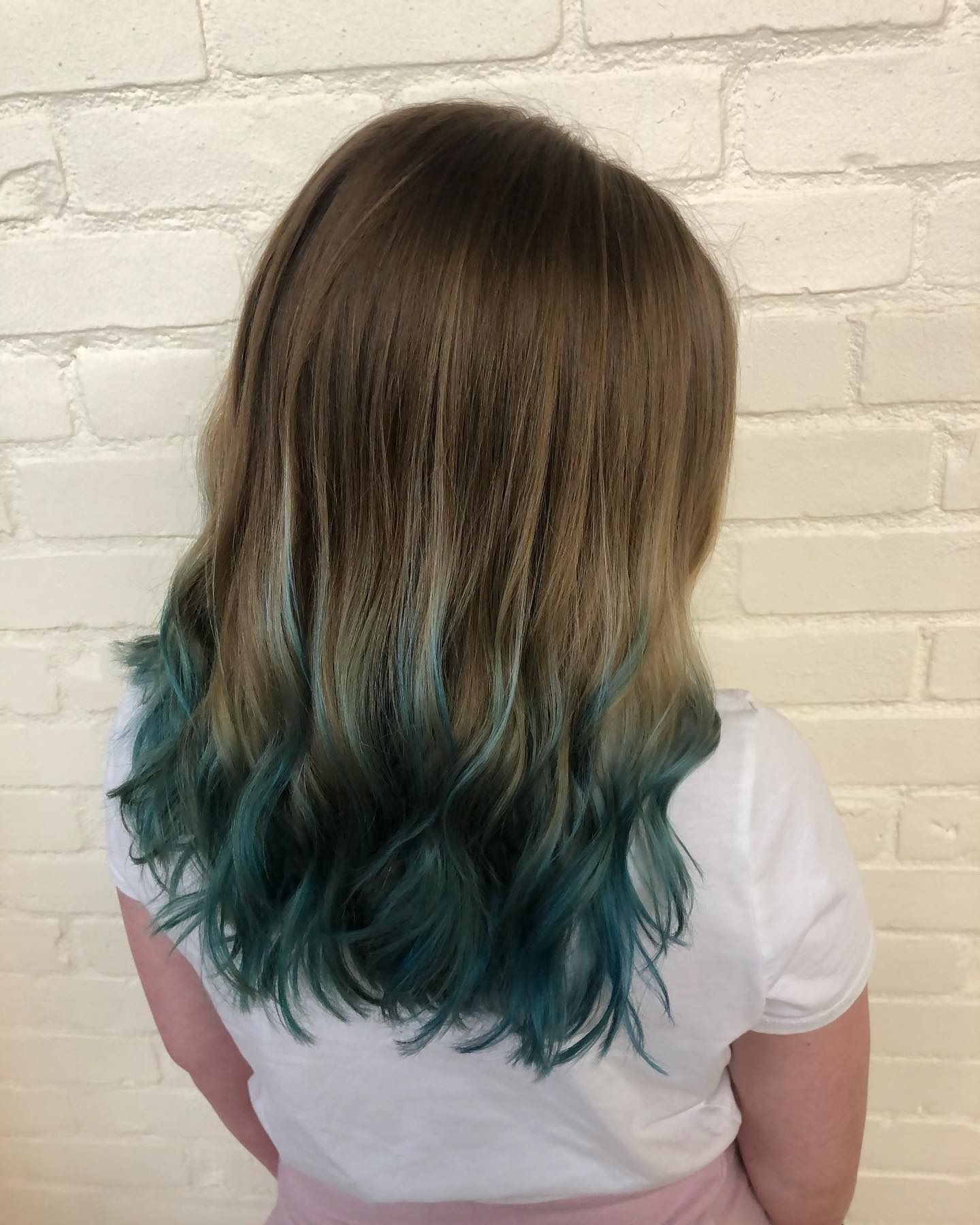 A woman with blue hair is standing in front of a white brick wall.