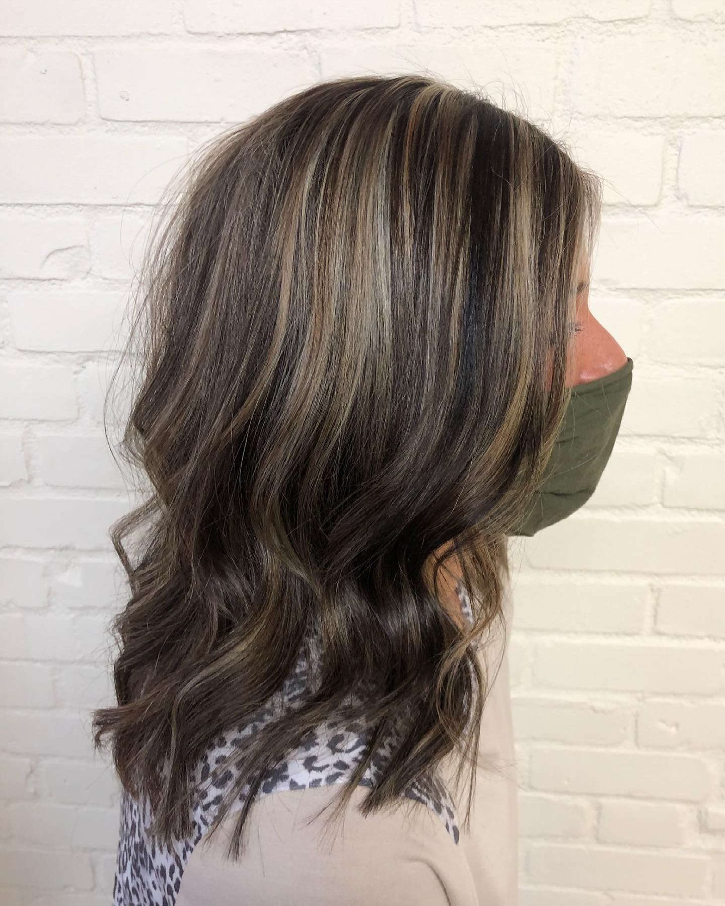 A woman wearing a mask and a leopard print shirt is standing in front of a white brick wall.