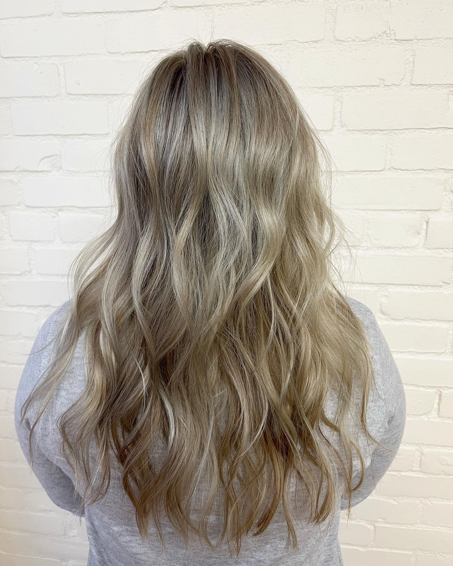 A woman with long blonde hair is standing in front of a white brick wall.