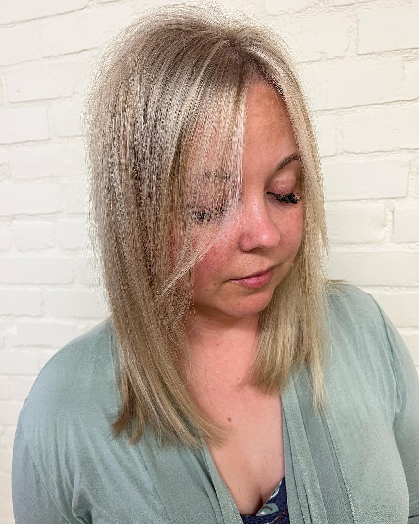 A woman with blonde hair and a green sweater is standing in front of a white brick wall.
