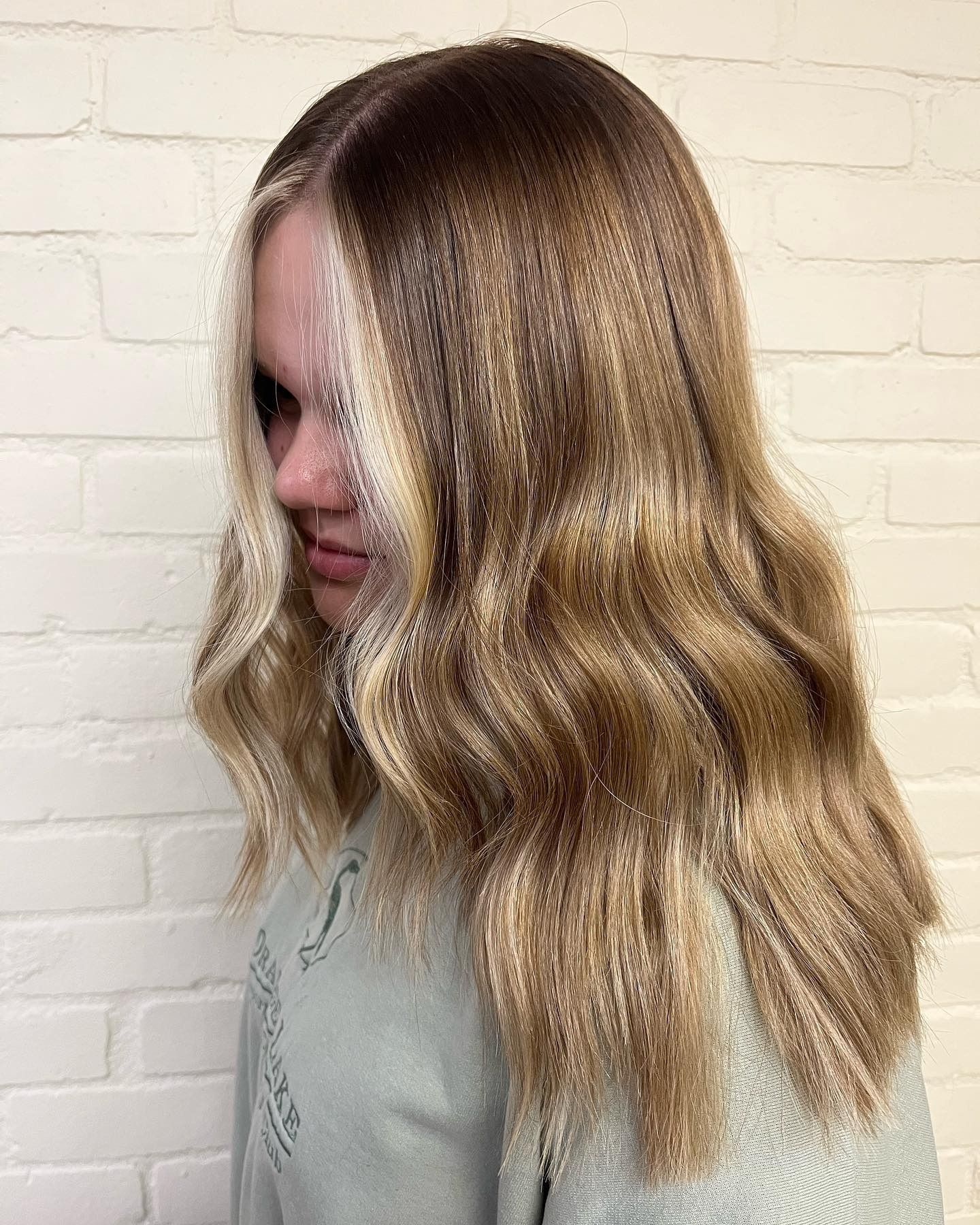 A woman with long blonde hair is standing in front of a white brick wall.