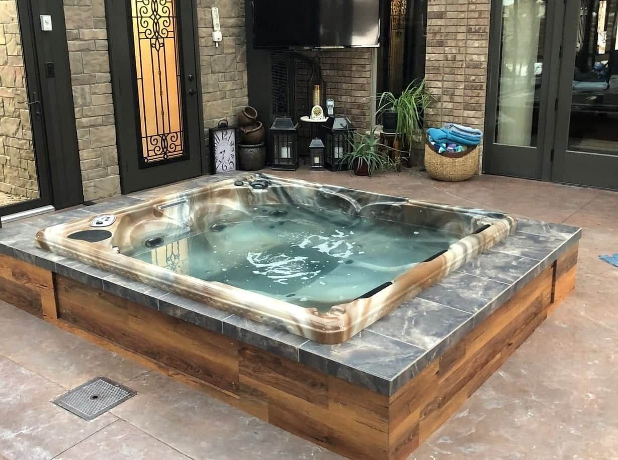 A hot tub is sitting on a tiled patio in front of a brick building.