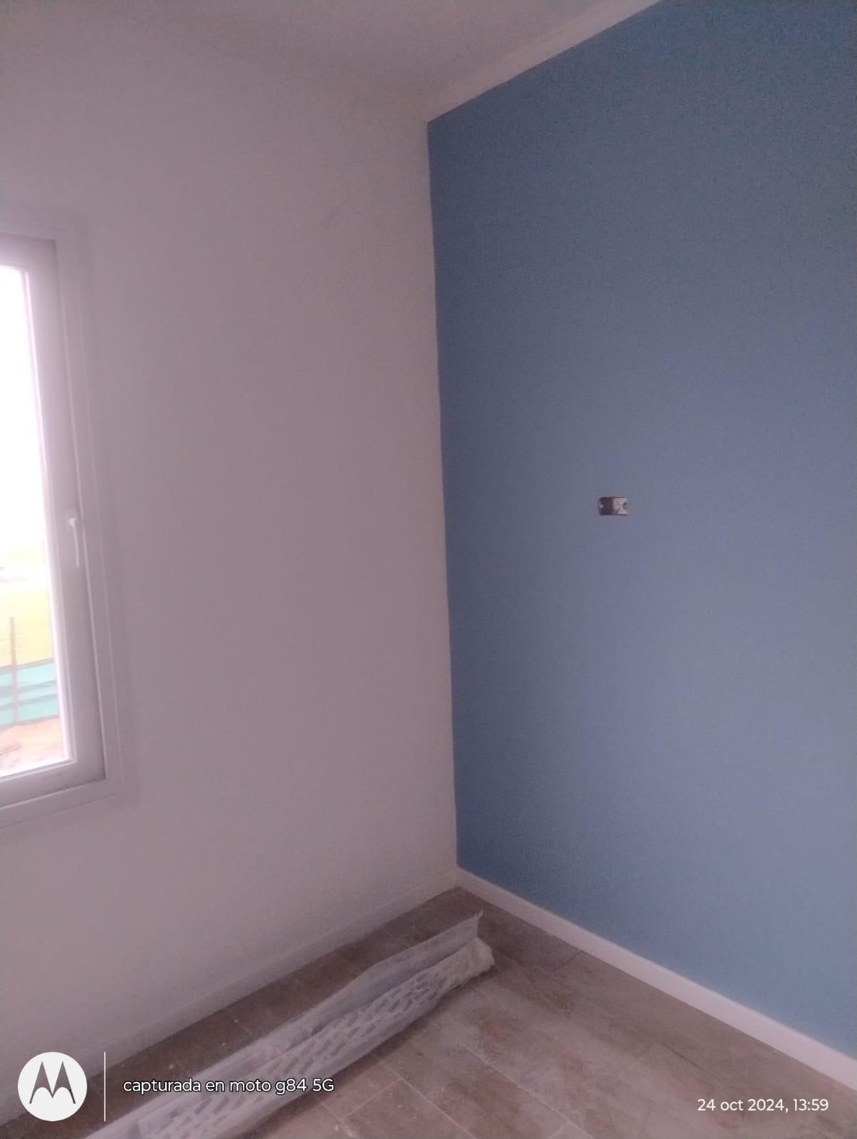 Una habitación pequeña con una pared azul y paredes blancas, una ventana y piso en proceso.