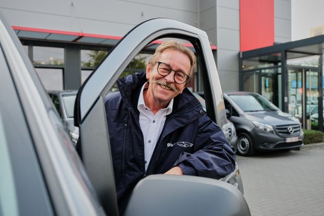 Foto van chauffeur die door het raam van zijn wagen naar de camera lacht.