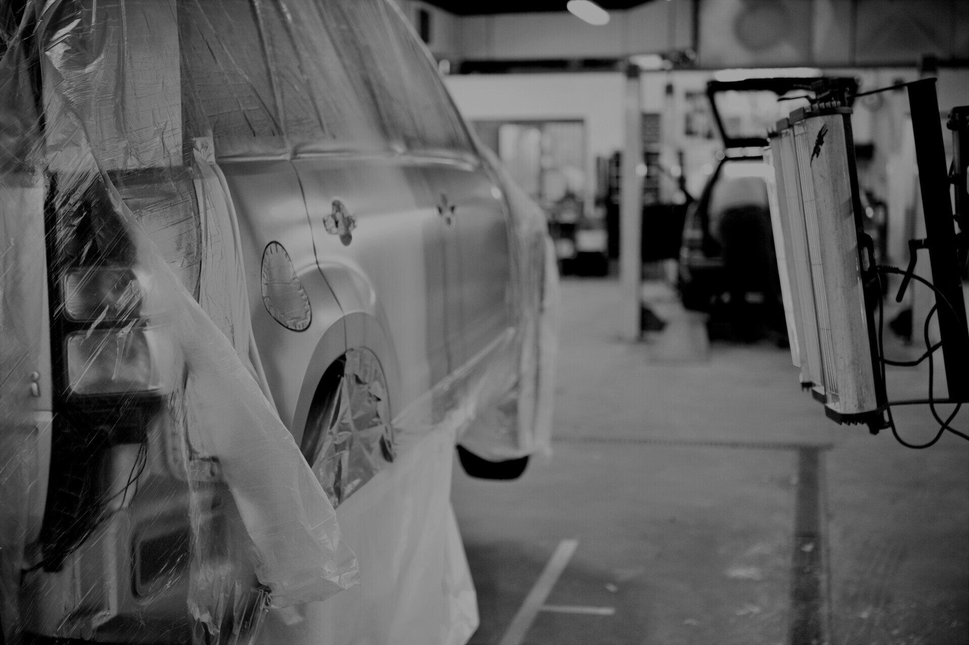 Foto van wagen die afgeplakt is en op een brug in de carrosserie staat, wachtend om met verf bespoten te worden.