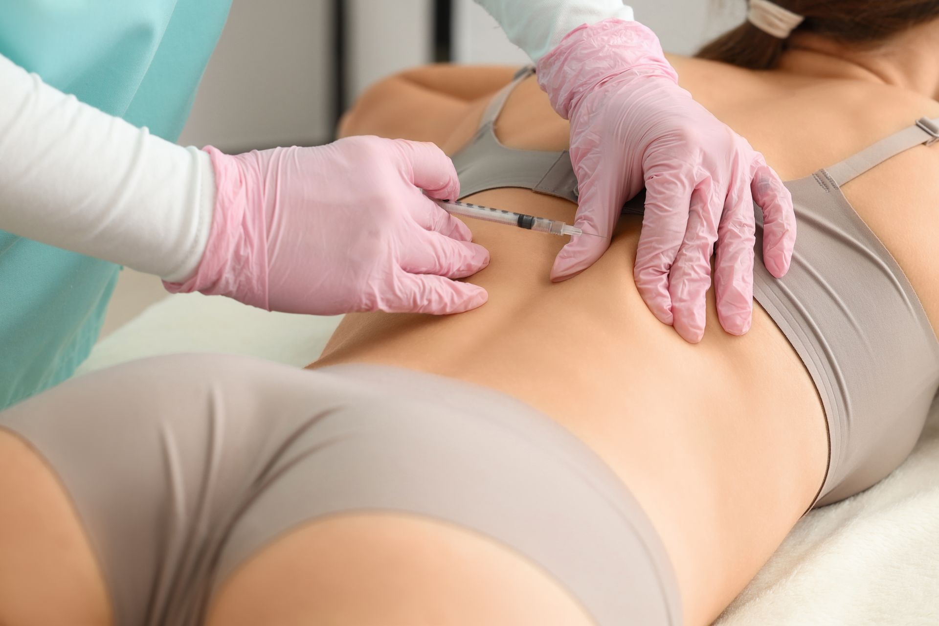 Person erhält Injektion in den unteren Rücken, behandschuhte Hände, medizinische Umgebung.