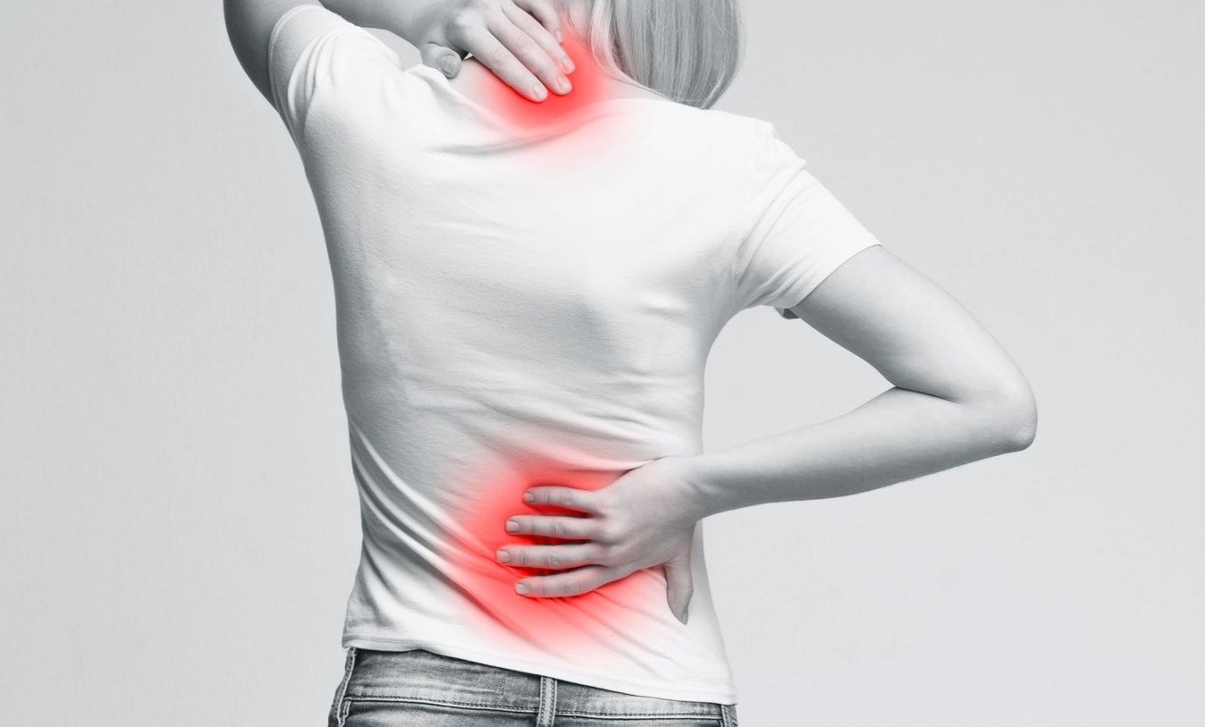 Frau in weißem Hemd mit roten Akzenten an Hals, oberem Rücken und unterem Rücken, die auf Schmerzen hindeuten.