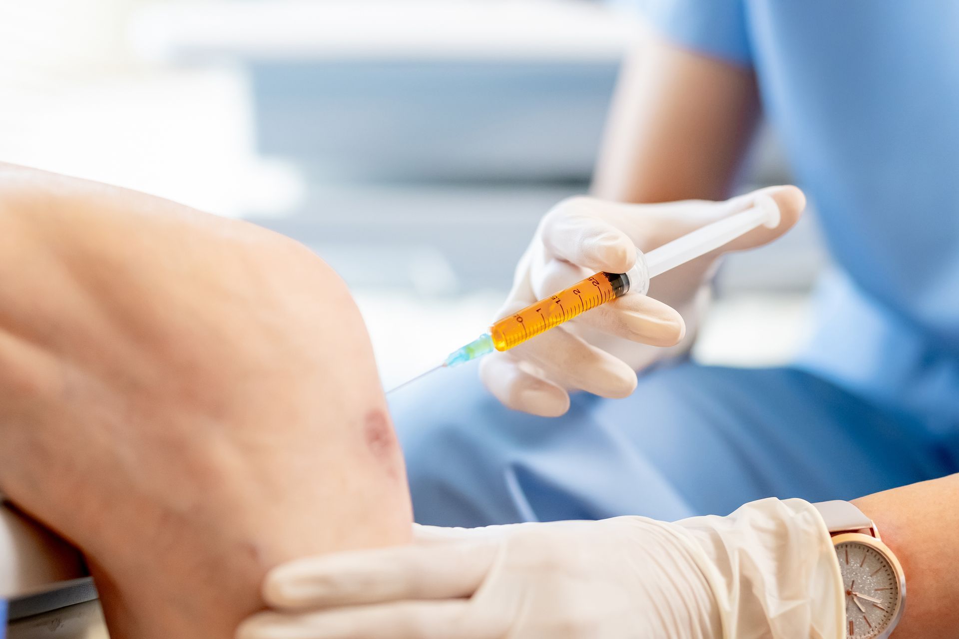 Eine Person, die in einer medizinischen Einrichtung von einem Mitarbeiter des Gesundheitswesens eine Knieinjektion erhält.
