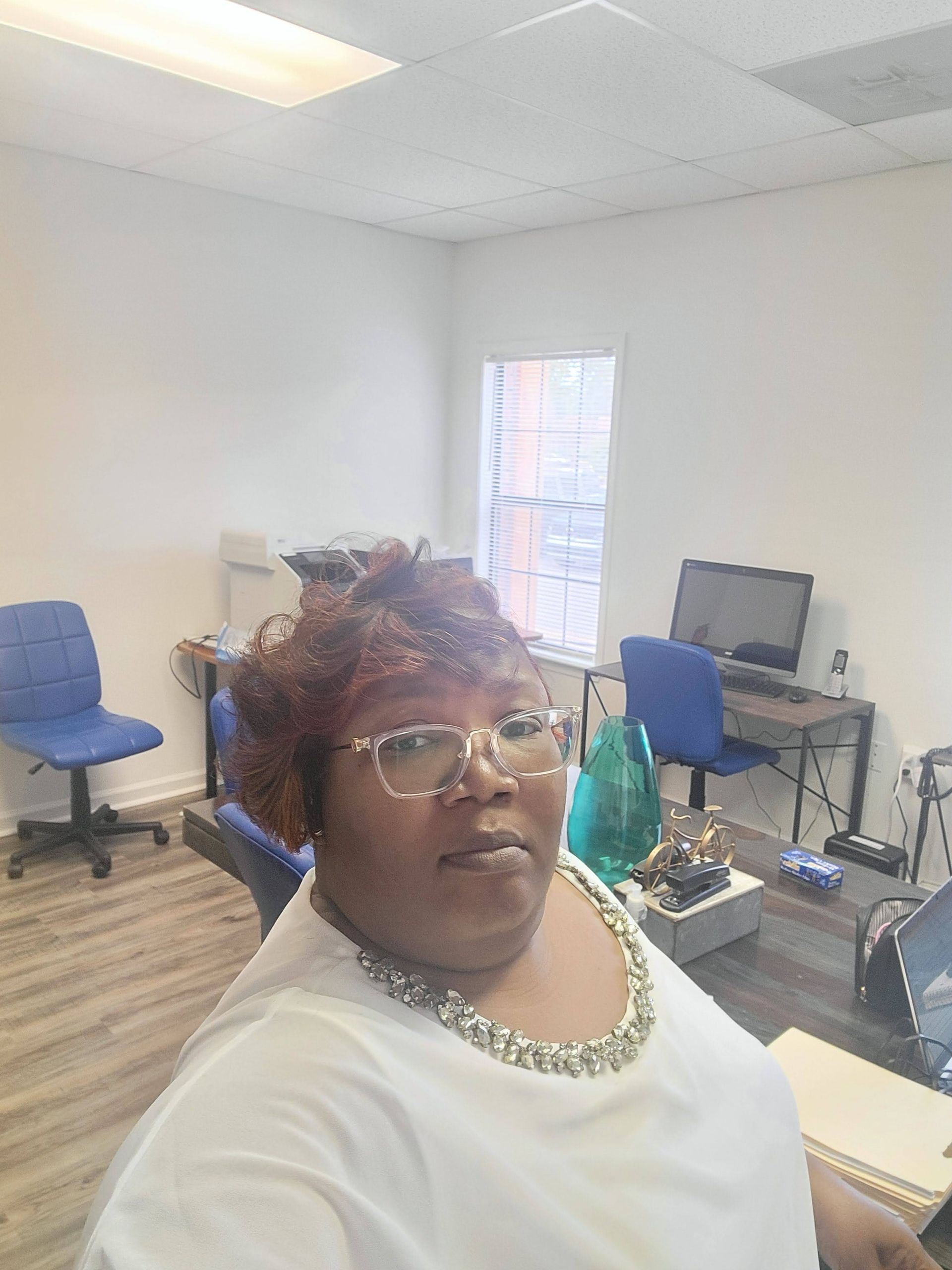 A woman is sitting at a desk with a laptop and a vase of flowers.