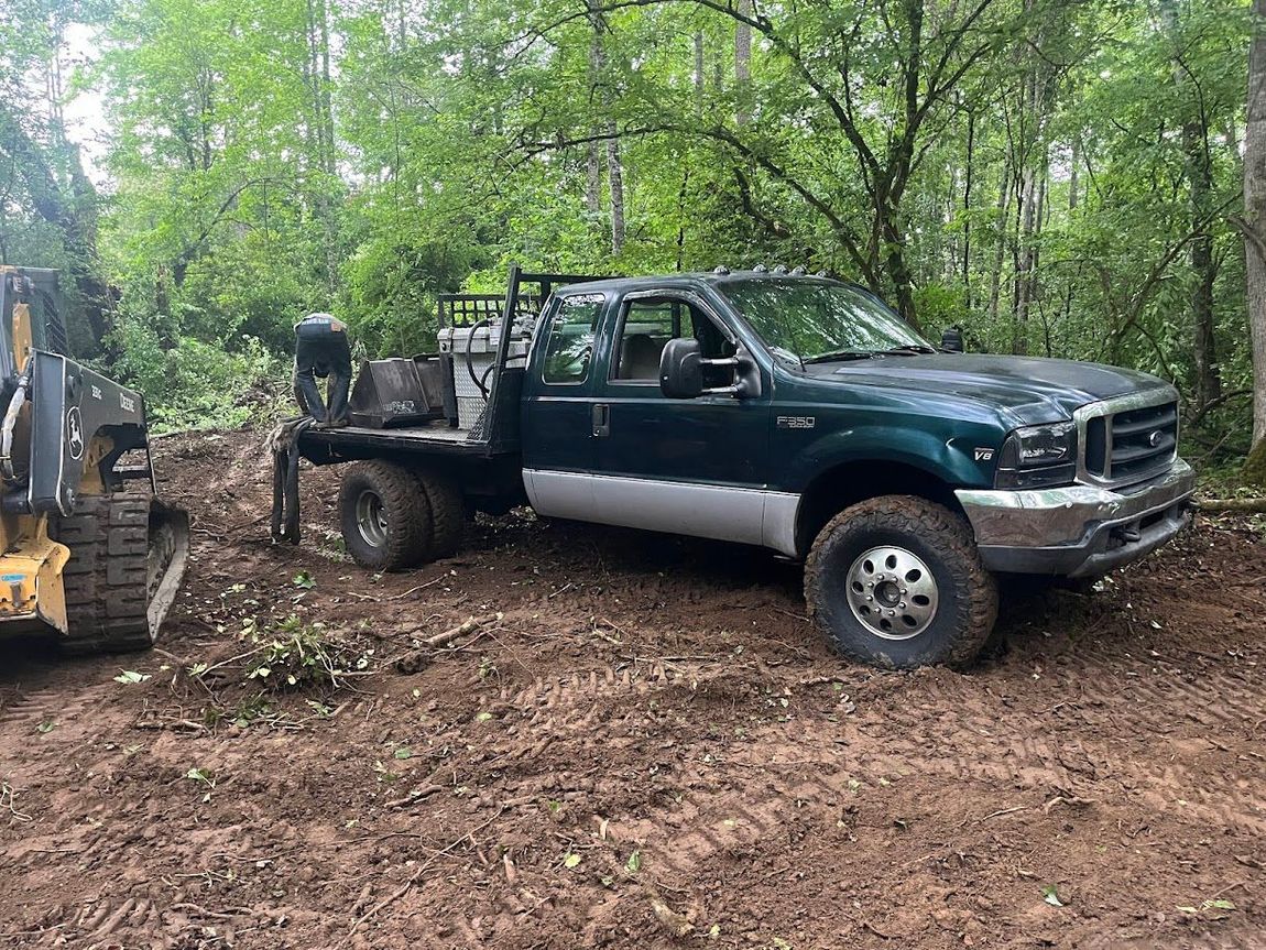 A truck is parked in the dirt next to a bulldozer.