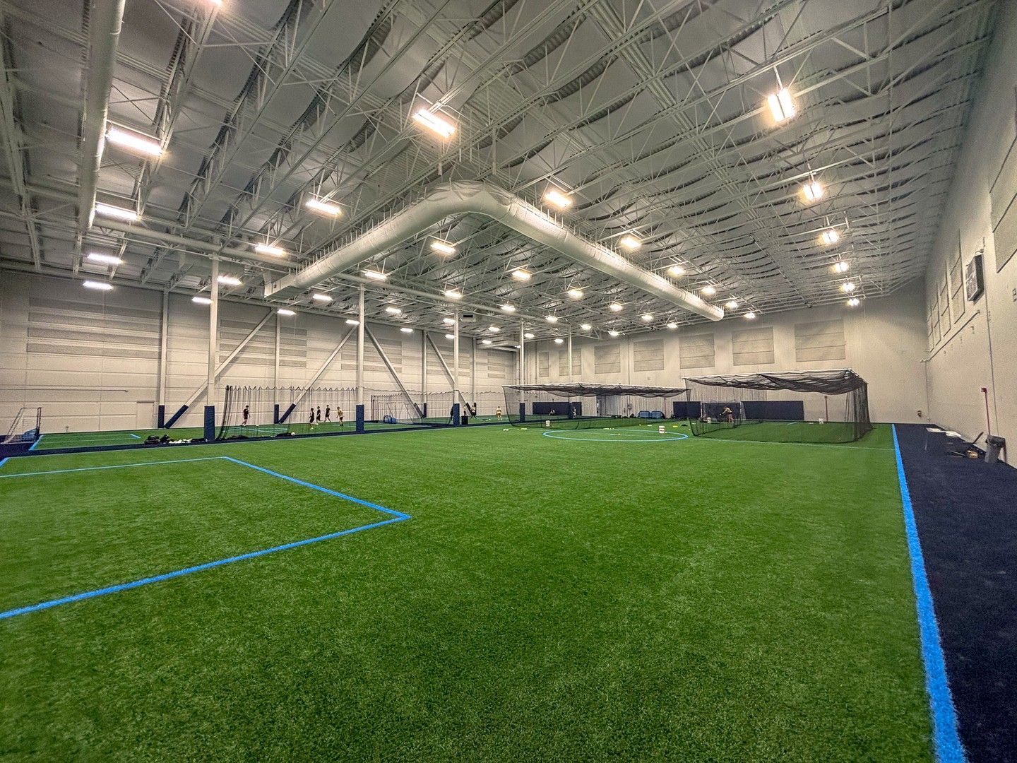 Indoor sports facility with green turf field, blue lines, and high ceiling.