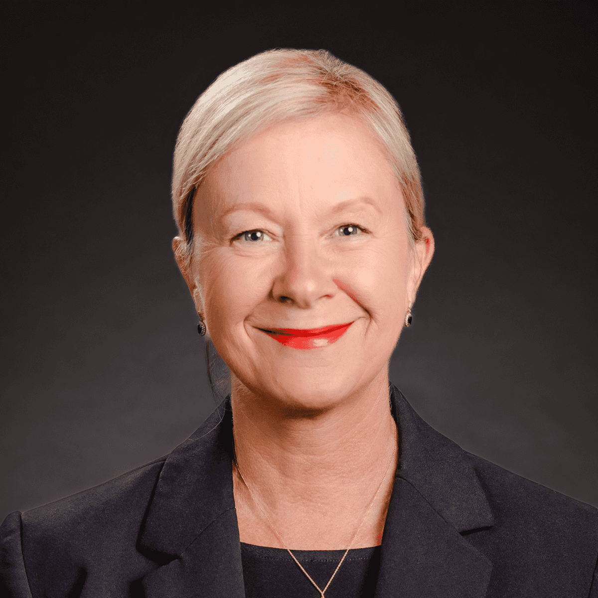 A woman in a suit and red lipstick is smiling for the camera.