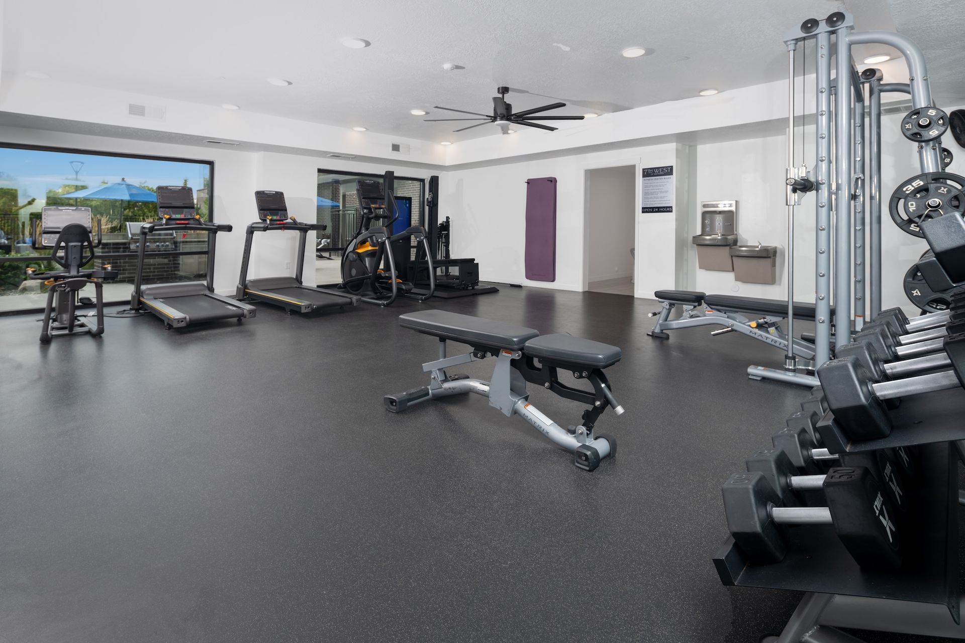 Gym with treadmills, weights, and weight machines. Black flooring, white walls.