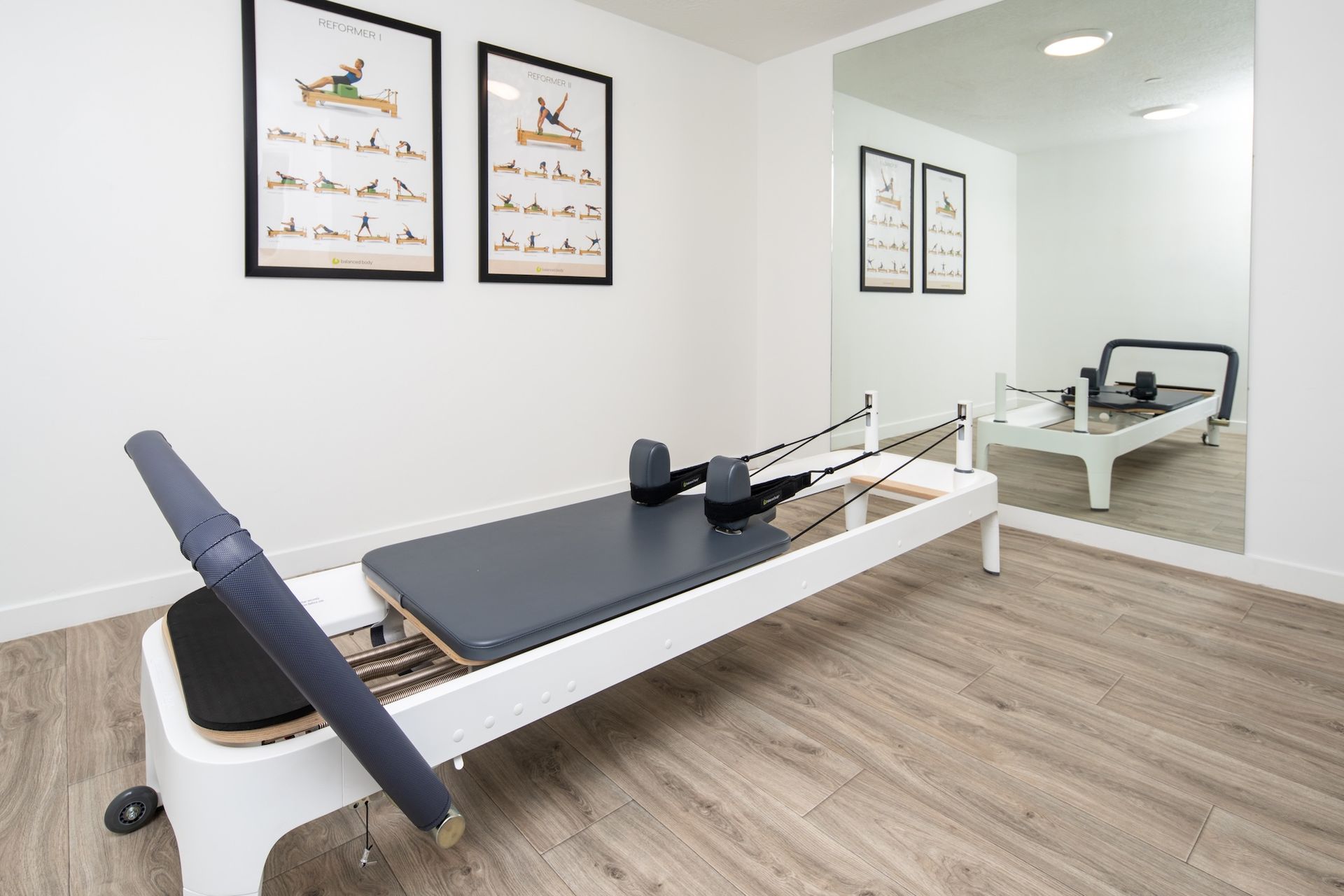 Pilates reformer in a bright room, with exercise diagrams and a mirrored wall.