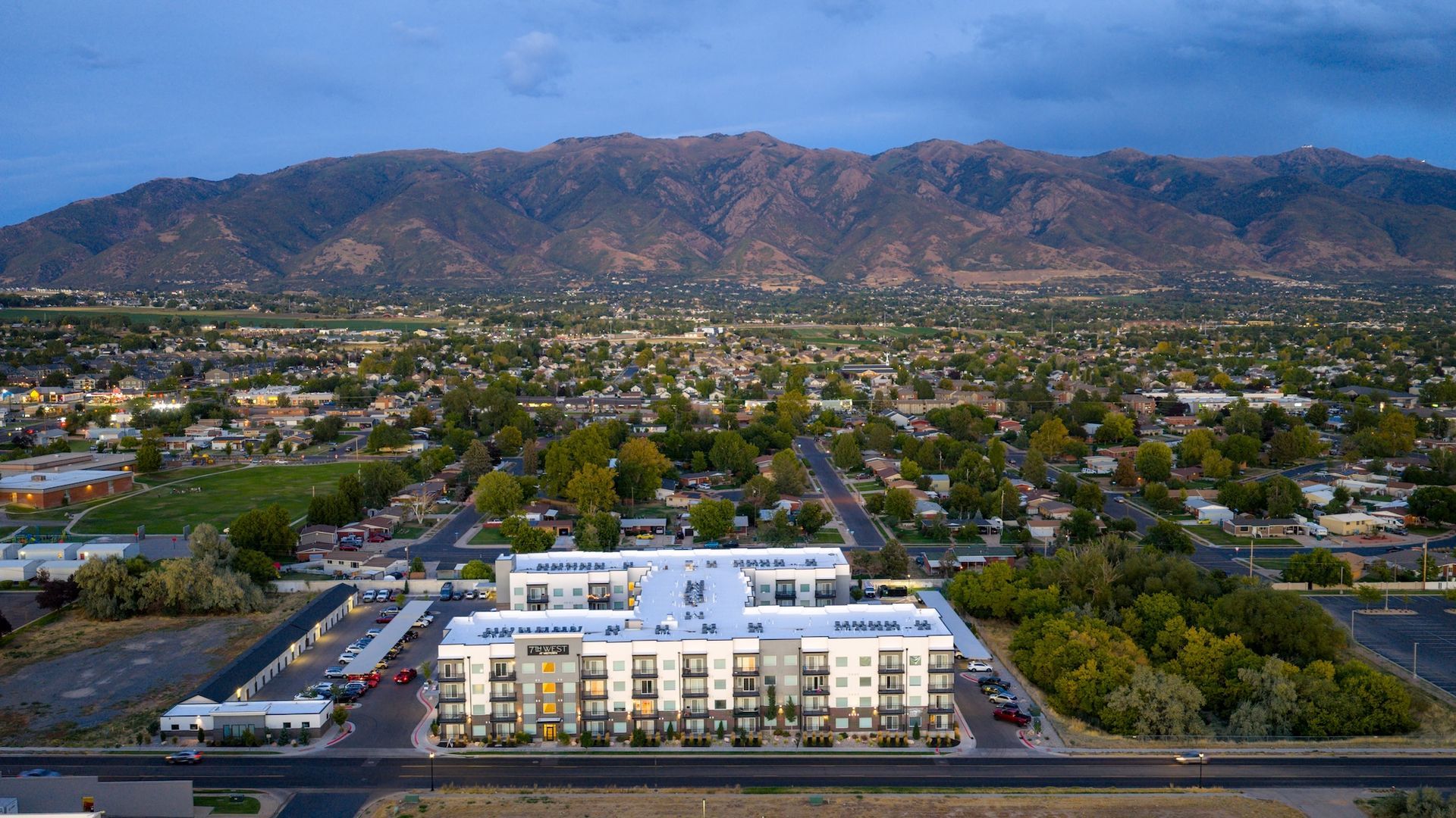 Aerial view of apartment complex with mountain backdrop at dusk.