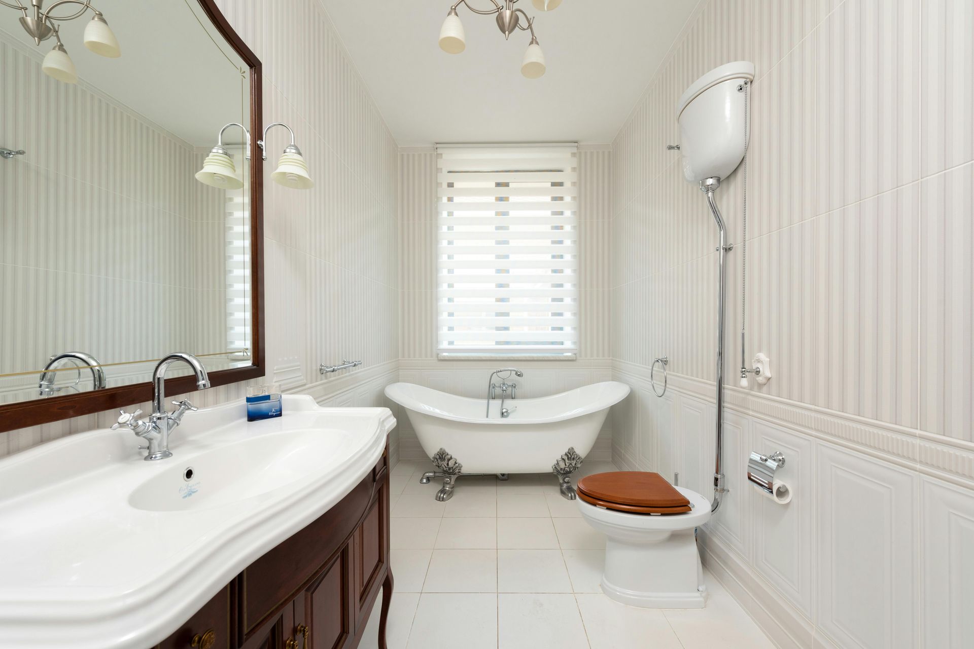 Bathroom with claw-foot tub, vintage toilet, large vanity, and striped wallpaper.