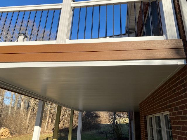 An elevated wooden deck with white railings and a finished white ceiling underneath, attached to a brick house exterior.
