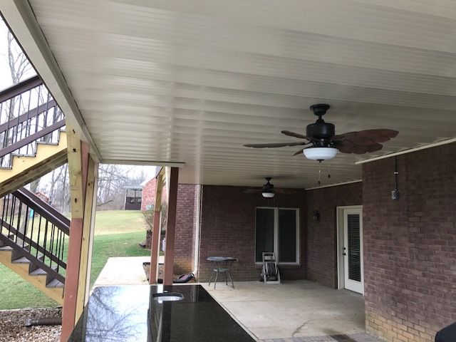 A covered brick patio features a granite-topped bar, two ceiling fans, and an adjacent wooden staircase.