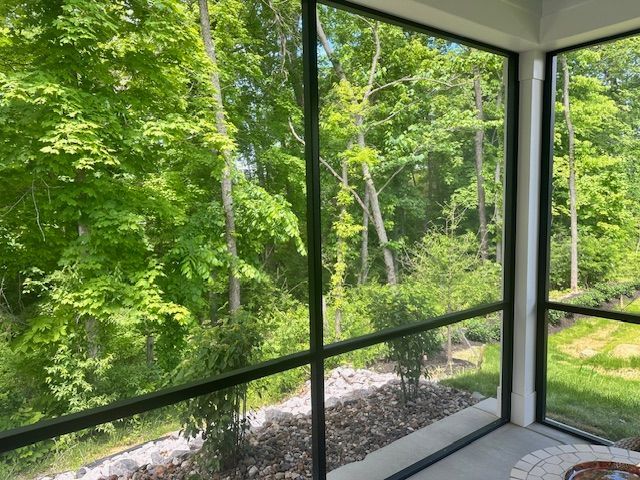 A screened-in porch looking out onto a bright, green woodland area with a rocky ground cover near the house.