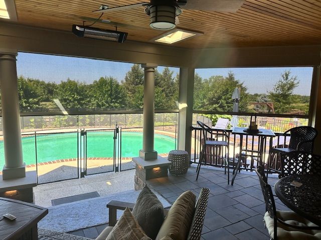A covered patio featuring seating, a ceiling fan, and a view of a backyard swimming pool enclosed by a fence.