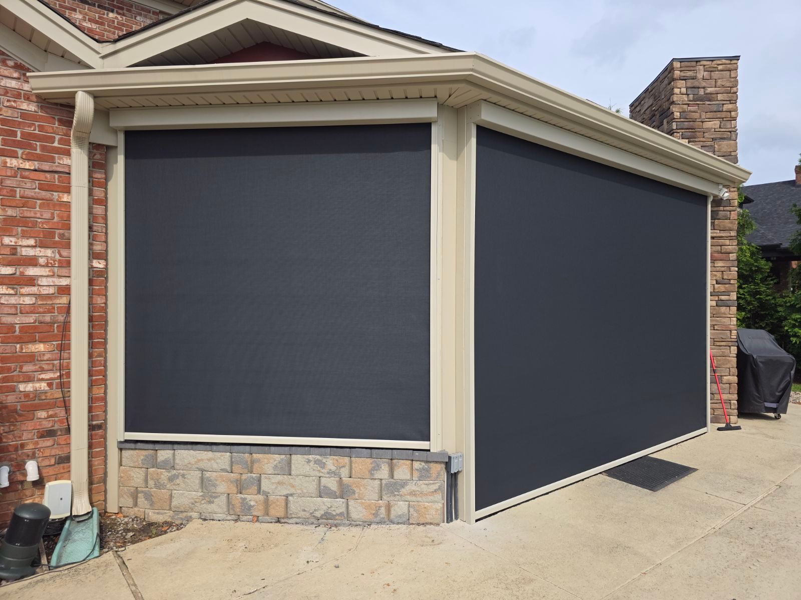 Two retractable outdoor privacy screens in charcoal grey installed on a covered brick patio.