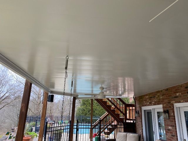 A covered outdoor patio with a smooth white ceiling, a ceiling fan, hanging chains, and a view of a pool area.