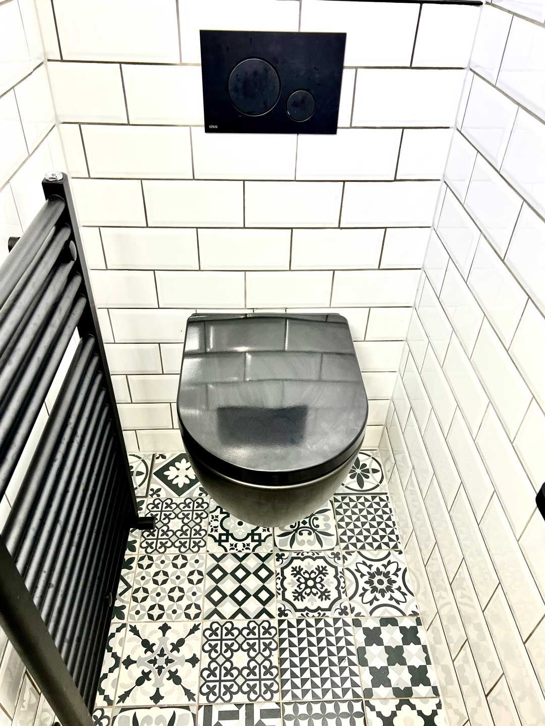 A toilet with a black seat and a black towel rack in a bathroom.