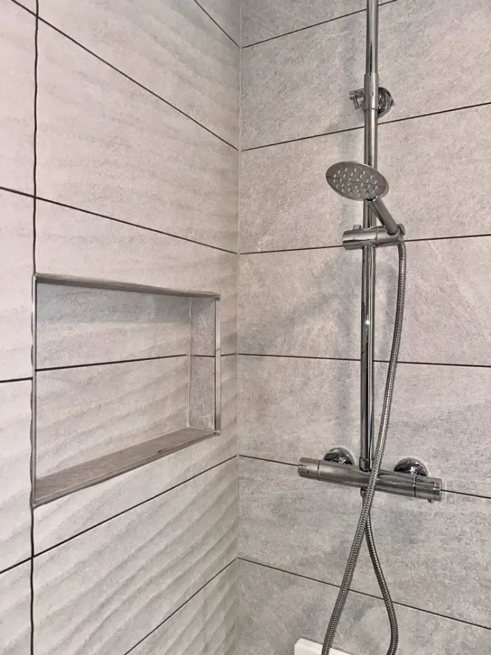 A shower head is sitting in a bathroom next to a shelf.