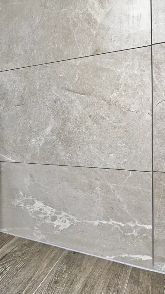 A close up of a tile wall next to a wooden floor.